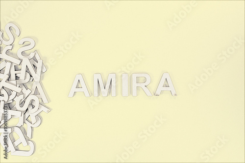 Popular and modern baby girl fashion name AMIRA in wooden English language capital letters spilling from a pile of letters on a yellow background pencil sketch photo