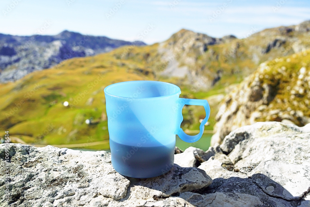 Rest during hiking: plastic mug with coffee standing on the edge of a cliff against the backdrop of scenic mountains. Moment from trekking in Montenegro (Kapetanovo Lake area, Niksic municipality) Rest during hiking: plastic mug with coffee standing on the edge of a cliff against the backdrop of scenic mountains. Moment from trekking in Montenegro (Kapetanovo Lake area, Niksic municipality)