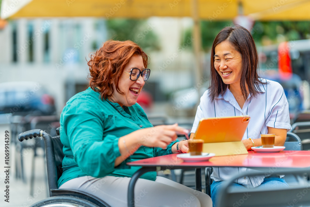 Woman with disability using tablet with friend at outdoor cafeteria