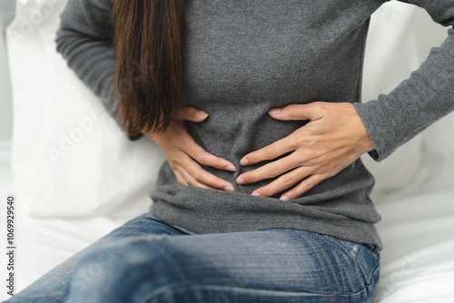 Suffer from stomach ache. asian young woman sitting on the bed feeling pain in stomach. photo