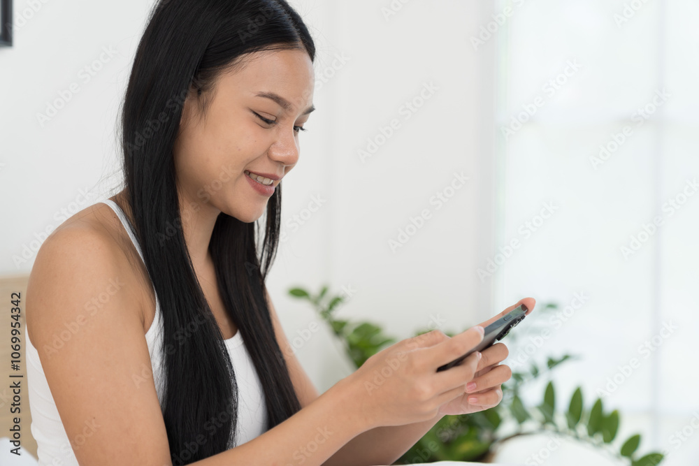 Cheerful young Asian woman playing games on mobile phone on bed in the bedroom Cheerful young Asian woman playing games on mobile phone on bed in the bedroom