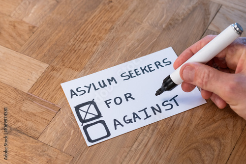 human hand with marker casts support vote on popular trending topic asylum seekers. public opinion varies around immigration, help, aid and shelter to be offered foreign nationals with refugee status photo
