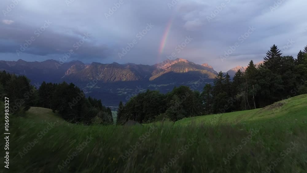 Drone rise above field reveal Mountain Landscape in Austria with Rainbow in Background