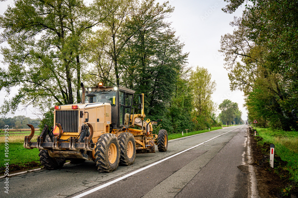 Motor grader spreading gravel at a construction site. Powerful road construction machinery for grading, leveling, and earthmoving. Ideal for infrastructure, civil engineering, and heavy projects. Motor grader spreading gravel at a construction site. Powerful road construction machinery for grading, leveling, and earthmoving. Ideal for infrastructure, civil engineering, and heavy projects.