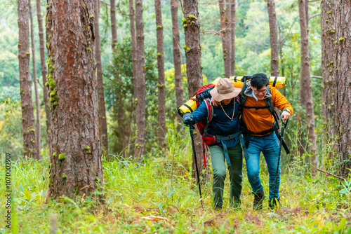 Two Asian man backpacker helping each other during hiking in forest mountain. People traveler enjoy adventure outdoor active lifestyle hiking on nature trail forest dirt road on holiday vacation.