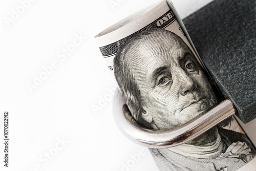 A close-up of a rolled U.S. one-hundred-dollar bill featuring Benjamin Franklin’s face, secured within a padlock. Concept of financial security, protection, and restricted access to wealth or savings.