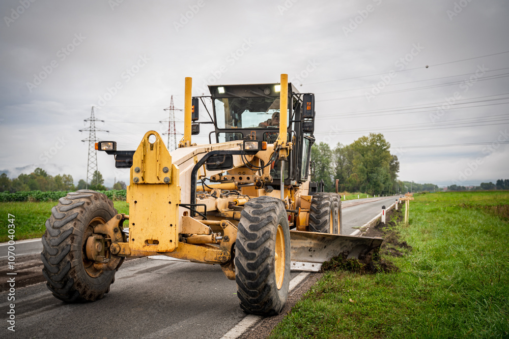Motor grader spreading gravel at a construction site. Powerful road construction machinery for grading, leveling, and earthmoving. Ideal for infrastructure, civil engineering, and heavy projects. Motor grader spreading gravel at a construction site. Powerful road construction machinery for grading, leveling, and earthmoving. Ideal for infrastructure, civil engineering, and heavy projects.