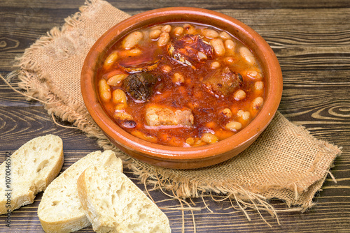 Clay casserole with Asturian fabada, surrounded by traditional ingredients such as garlic, bread and sausages. Typical dish of Spanish cuisine, ideal for gastronomy and traditional recipes photo