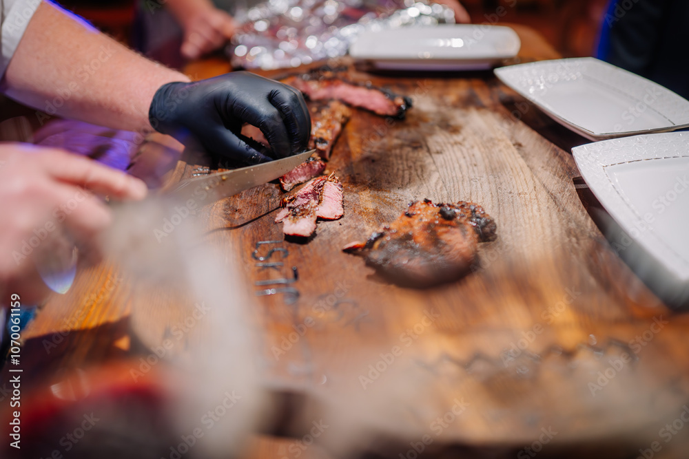 Obraz premium A chef slices grilled steak on a wooden board, preparing to serve on white plates. The steak is charred and juicy, with engraved details visible on the board..