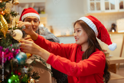 party, enjoying, decorating, couple, happy, celebrate, present, celebration, christmas, gift. A woman in a red sweater is decorating a Christmas tree. They are smiling and seem to be enjoying.