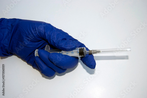 A hand in a blue glove with a syringe.  A medical hand holding a disposable syringe. A doctor's or nurse's hand in a glove isolated on white. Vaccination or medical treatment.