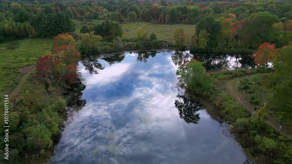 Aerial panoramic dolly above pond with calm water reflecting textured sky and clouds in middle of green forest Aerial panoramic dolly above pond with calm water reflecting textured sky and clouds in middle of green forest