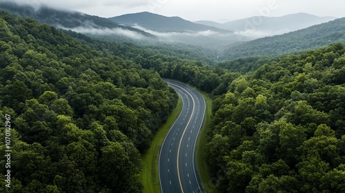 Drone view of a scenic mountain highway in a dense forest, misty hills in the background, peaceful and moody environment