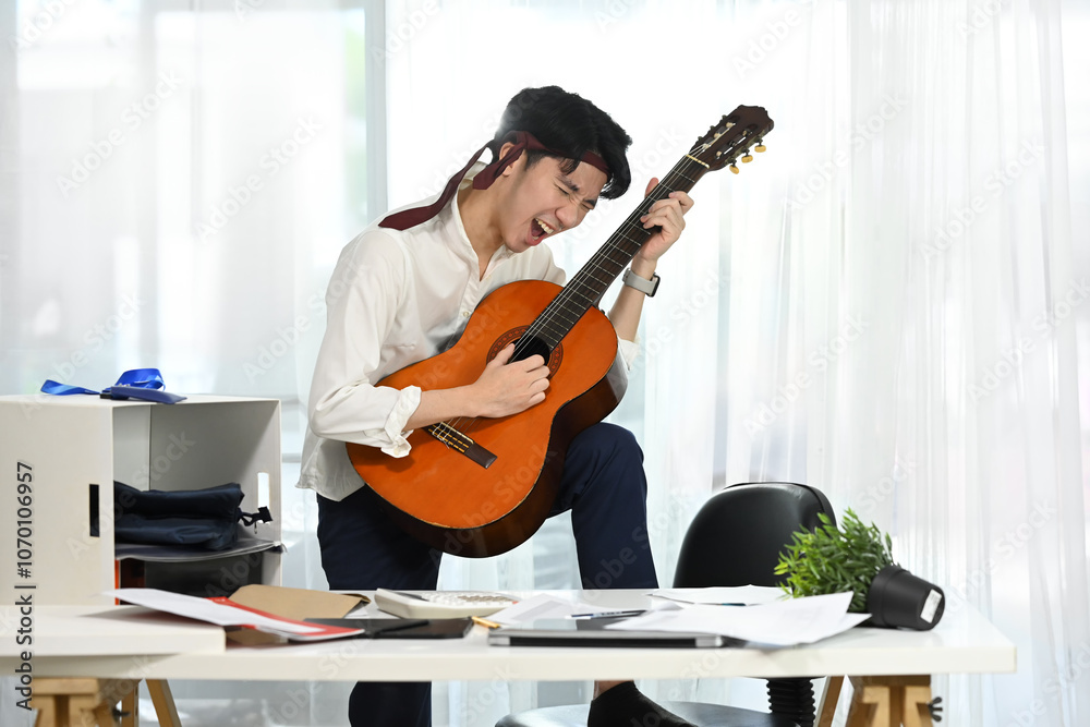 Fototapeta premium Joyful employee playing guitar during break at the workplace