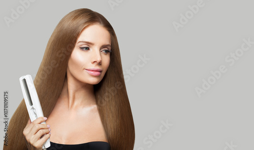 Gorgeous brunette woman holding straight hair iron and straightening her long smooth shiny hair on white background. Haircare, hairstyle, hairdressing and hair styling concept