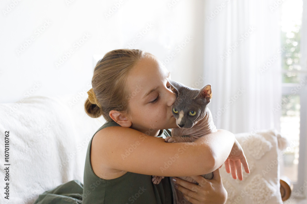 Obraz premium Cute young happy child girl embracing lovely Sphynx cat pet of a hairless breed at home, lifestyle portrait