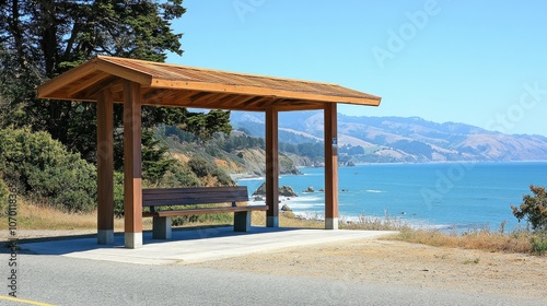 Simple wooden bus stop along a coastal road, with ocean waves in the background under clear skies.