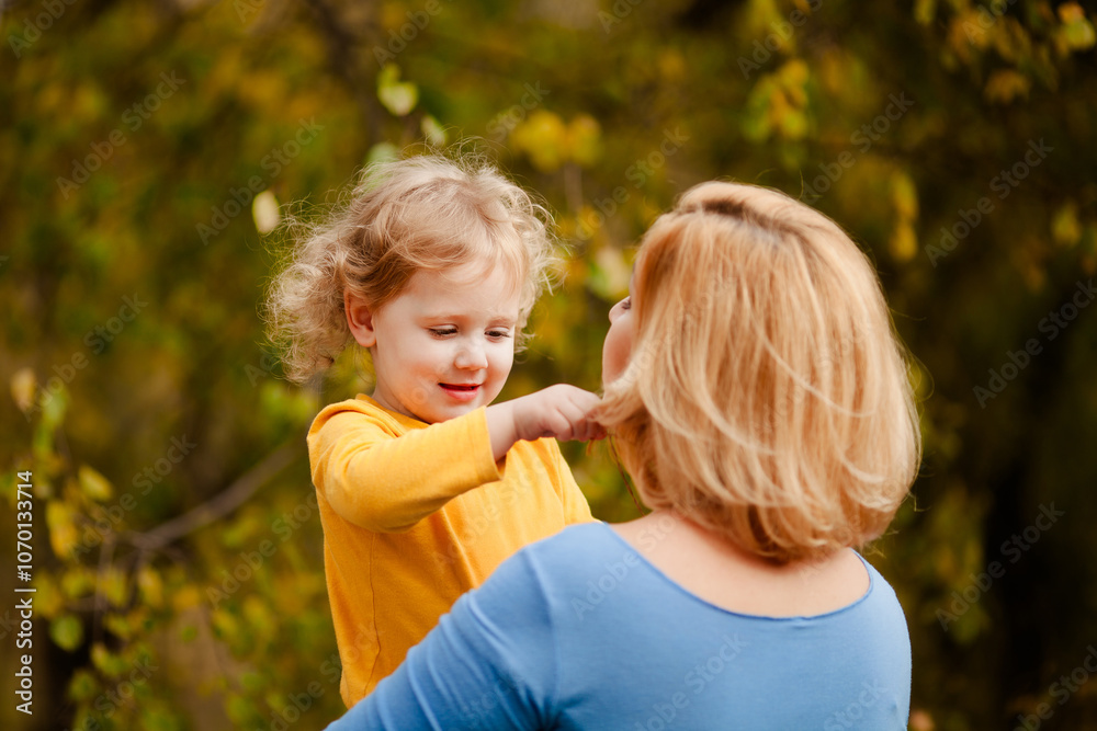 Loving mother holding toddler girl with curly hair in yellow shirt in autumn park Loving mother holding toddler girl with curly hair in yellow shirt in autumn park