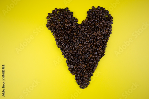Coffee beans arranged in the shape of a heart on a yellow background