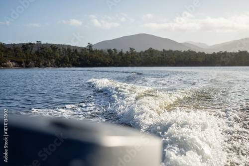 tinny dinghy boat on the water making a wake behind a boat making waves on a river in a national park in australia. beach in summer, dingy going fast photo