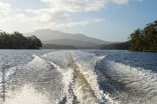 tinny dinghy boat on the water making a wake behind a boat making waves on a river in a national park in australia. beach in summer, dingy going fast