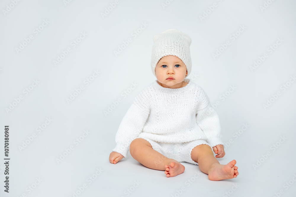 A baby boy on a white isolated background with a place for text is sitting in white knitted clothes with a hat. A small child in a winter sweater, space for text A baby boy on a white isolated background with a place for text is sitting in white knitted clothes with a hat. A small child in a winter sweater, space for text