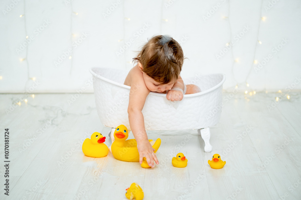 A baby boy is bathing in a bubble bath and playing with rubber ducklings for bathing on a white isolated background with a place for text. A small happy child washes the space for text. A baby boy is bathing in a bubble bath and playing with rubber ducklings for bathing on a white isolated background with a place for text. A small happy child washes the space for text.