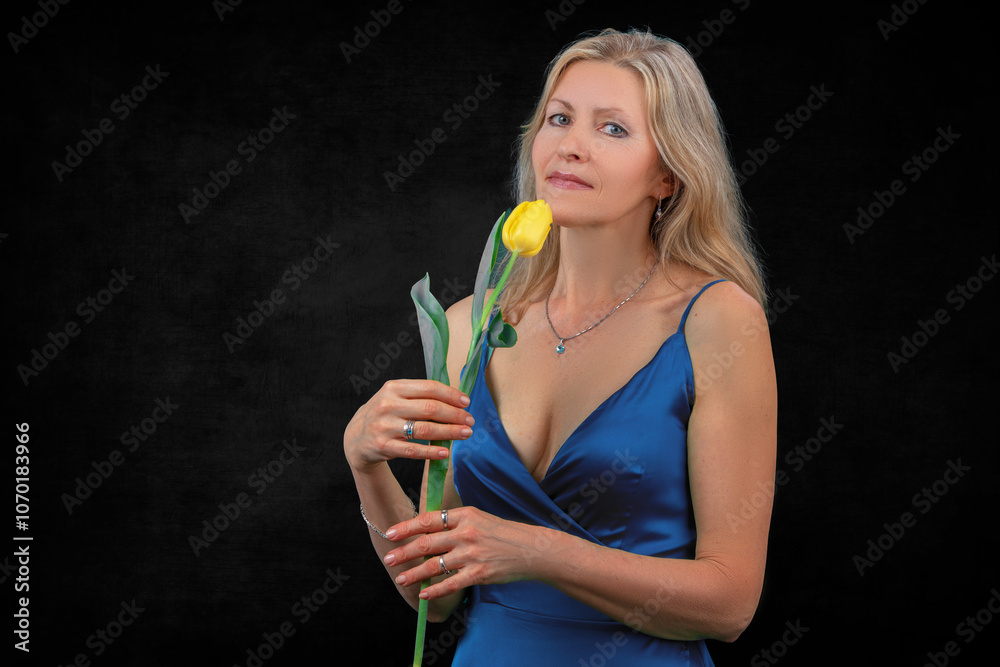A beautiful adult woman holds a yellow tulip on a dark background. A beautiful adult woman holds a yellow tulip on a dark background.