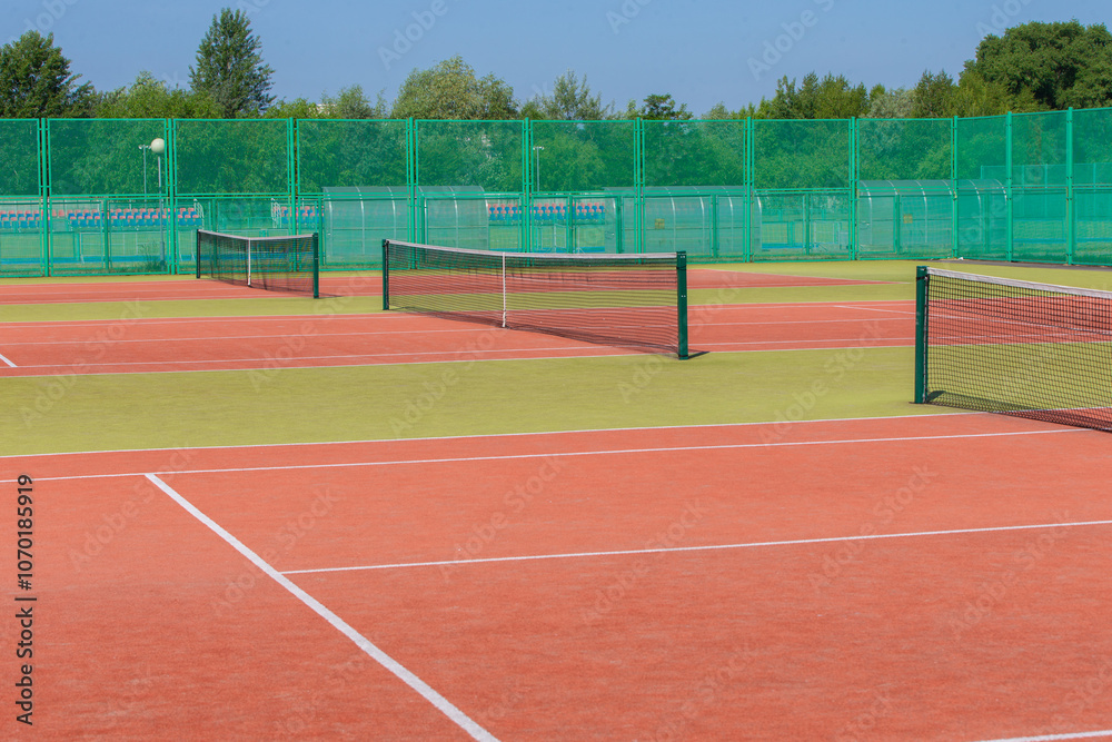 Fototapeta premium The tennis court is empty with a net and a green fence.