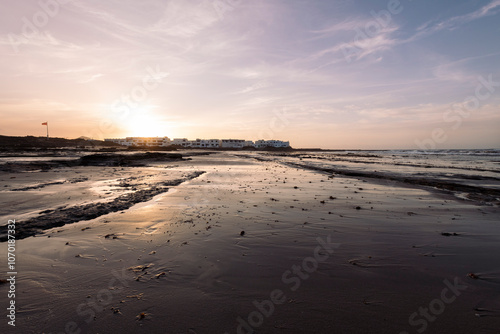 Wallpaper Mural volcanic beach of Famara against ocean with houses at sea coast under cloudy sky at sunset in Teguise, Lanzarote at Canary Islands in Spain, concept of wild nature and marine landscape Torontodigital.ca