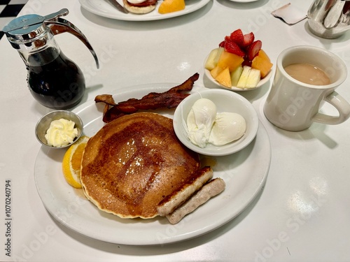 A Typical American breakfast with pancakes, sausage, bacon, egg, maple syrup and coffee on a white table. 