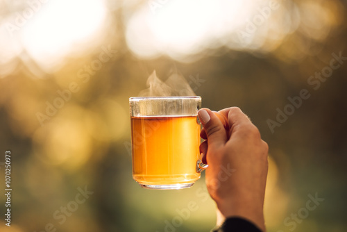 Foto A glass of hot herbal tea with steam in a woman's hand outdoors.