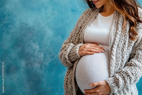 A pregnant woman cradles her belly in front of a blue wall
