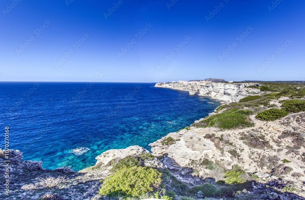 Historic Bonifacio on Corsica’s dramatic limestone cliffs against a clear blue Mediterranean sea and sky