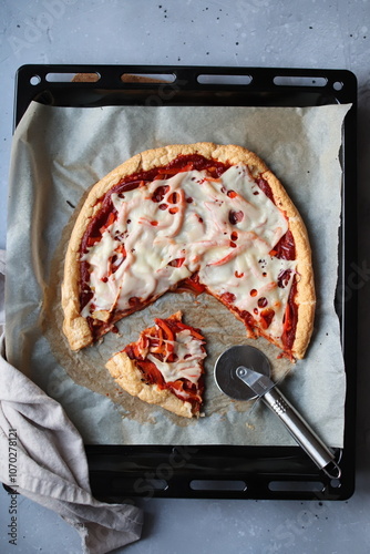 Pizza z sosem pomidorowym i serem krojona na blasze z papierem do pieczenia z nożem do pizzy