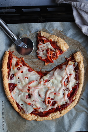 Pizza z sosem pomidorowym i serem krojona na blasze z papierem do pieczenia z nożem do pizzy