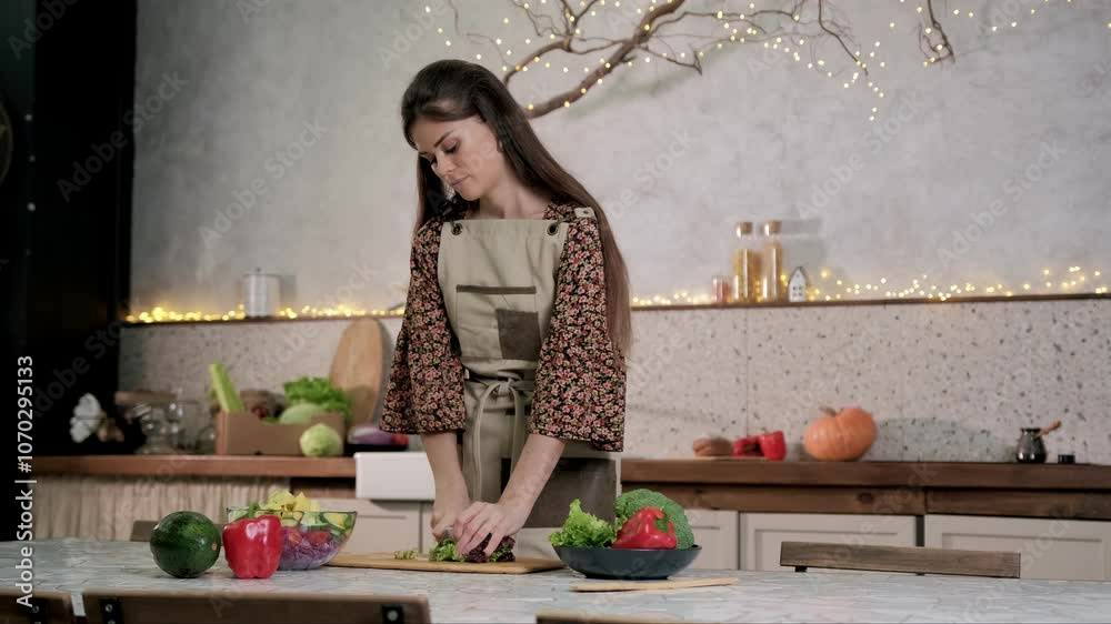 Woman wearing an apron is carefully chopping vegetables on a kitchen counter. Preparing healthy meal in a cozy and comfortable kitchen space, fresh and delicious ingredients. raw vegetables. person
