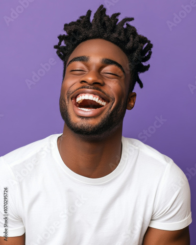 A young man laughing joyfully, dressed casually, set against a pastel purple background.