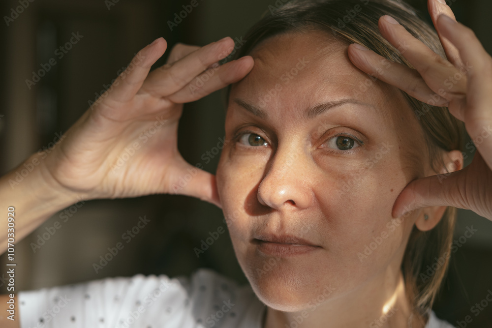 Portrait of beautiful mature woman touching her skin and looking at camera. Close-up face of middle aged woman with wrinkles, massaging her face. Aging process concept. Portrait of beautiful mature woman touching her skin and looking at camera. Close-up face of middle aged woman with wrinkles, massaging her face. Aging process concept.