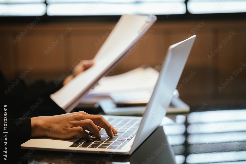 Fototapeta premium Young Asian businesswoman pointing pen with graph and chart report and using laptop computer to analyze data.