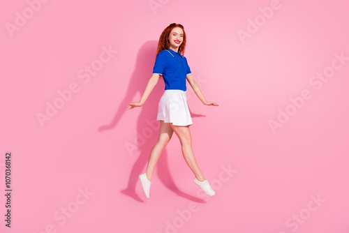 Full length photo of adorable lovely girl wear short skirt jumping high walking empty space isolated pink color background