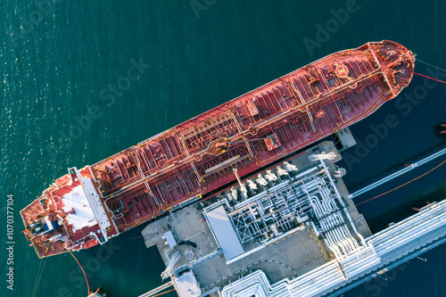 Aerial top down view of a large oil tanker docked at a pier in the port in process of loading.