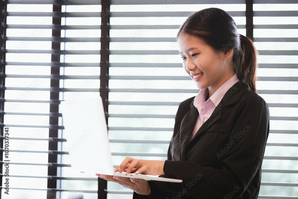 Young Asian woman in suit using laptop by window in office. Close-up of body. Copy space available. Young Asian woman in suit using laptop by window in office. Close-up of body. Copy space available.