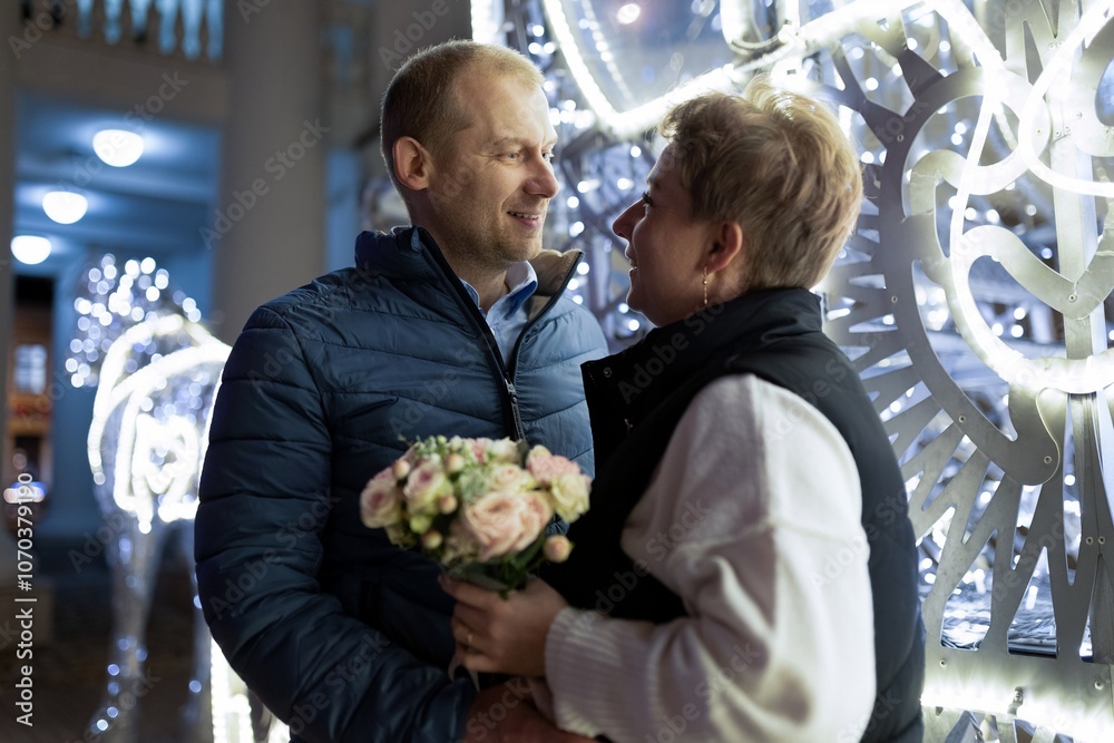A couple walks through a city at night, the man holding a bouquet of flowers A couple walks through a city at night, the man holding a bouquet of flowers