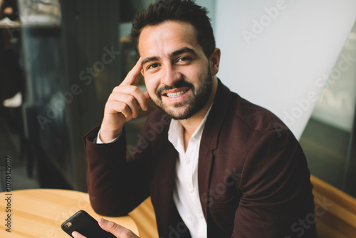 Portrait of handsome smiling businessman in formal wear using mobile phone for chatting online having break in cafe interior, positive successful male entrepreneur looking at camera enjoy devices