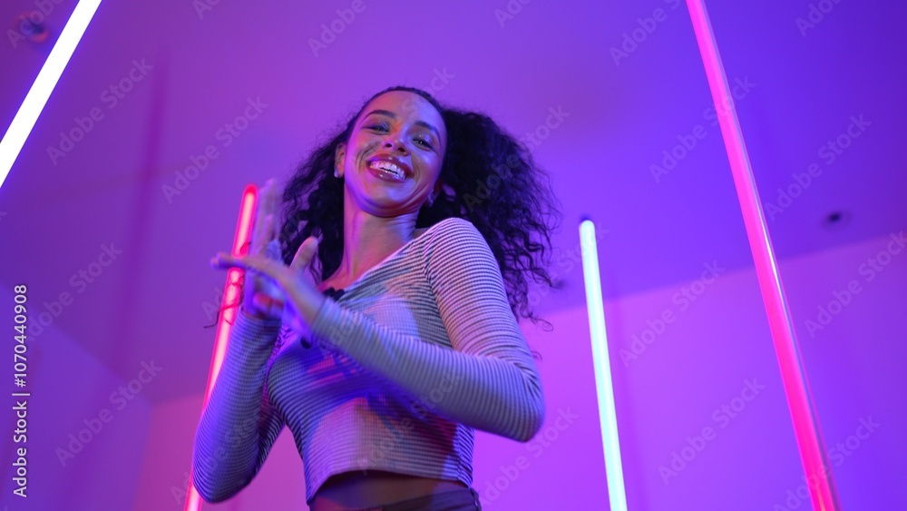 Low angle camera of hispanic dancer looking at camera and dancing to city pop music. Professional attractive hipster moving to hip hop song with purple led or neon light. Stylish cloth. Regalement. Low angle camera of hispanic dancer looking at camera and dancing to city pop music. Professional attractive hipster moving to hip hop song with purple led or neon light. Stylish cloth. Regalement.