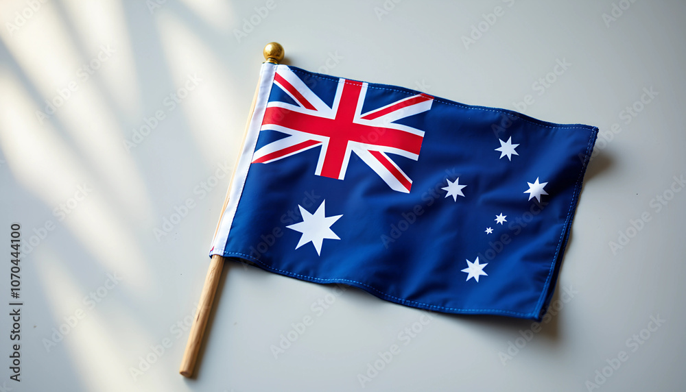 Fototapeta premium Australian flag displayed on a wooden stick against a neutral background in bright daylight
