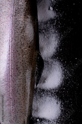 Fresh whole rainbow trout on black background with salt. Close-up. Copy space. Top view