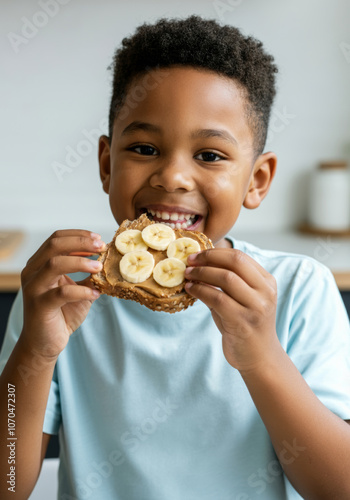 Joyful African-American child eating peanut butter and banana sandwich in bright kitchen.