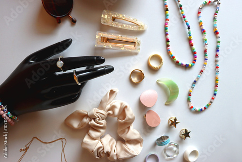 Hand figurine, sunglasses, gold jewelry, colorful bead jewelry, statement rings and various hair accessories on the white table. Flat lay.
